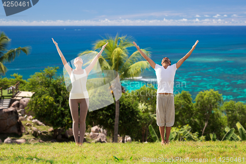 Image of happy couple making yoga exercises on beach