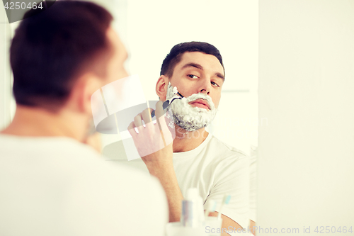 Image of man shaving beard with razor blade at bathroom