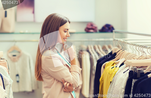 Image of happy young woman choosing clothes in mall