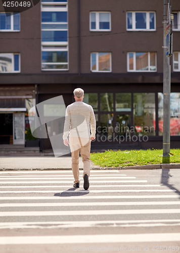 Image of senior man walking along city crosswalk