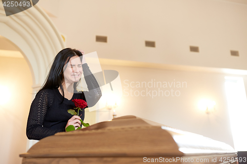 Image of crying woman with red rose and coffin at funeral