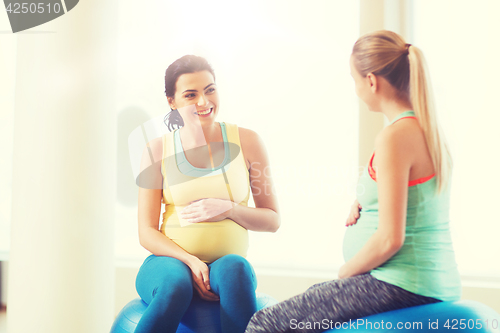 Image of two happy pregnant women sitting on balls in gym