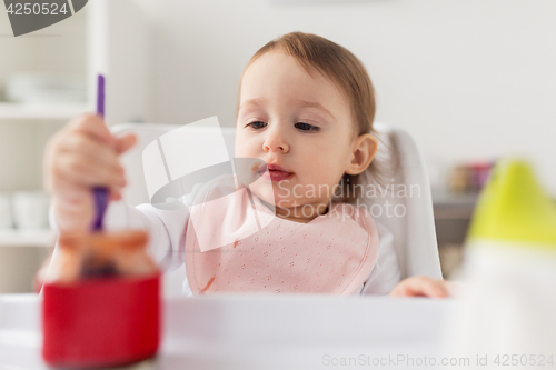 Image of baby girl with spoon eating puree from jar at home