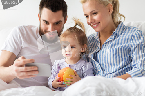 Image of happy family with smartphone in bed at home