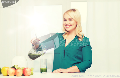 Image of happy woman with blender jug pouring juice at home