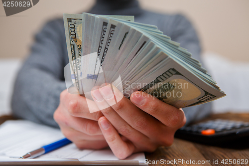 Image of Caucasian hands counting dollar banknotes on dark wooden table