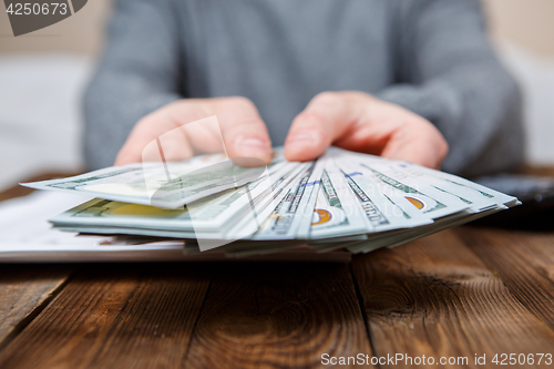 Image of Caucasian hands counting dollar banknotes on dark wooden table