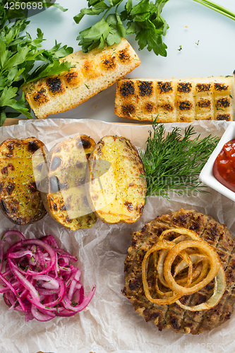 Image of burger grill with vegetables, sauce on a wooden surface. potatoes and bread