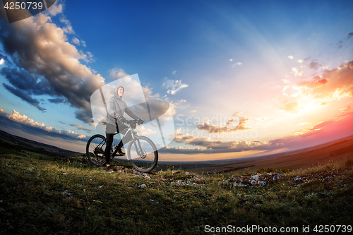 Image of Young man cycling on a rural road through meadow