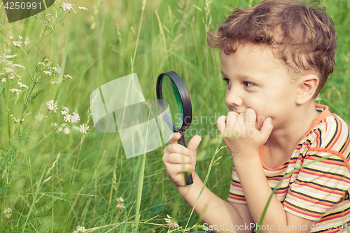 Image of Happy little boy exploring nature with magnifying glass