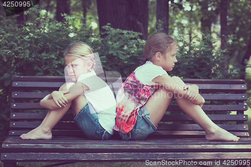 Image of two sad sister sitting on the bench in park