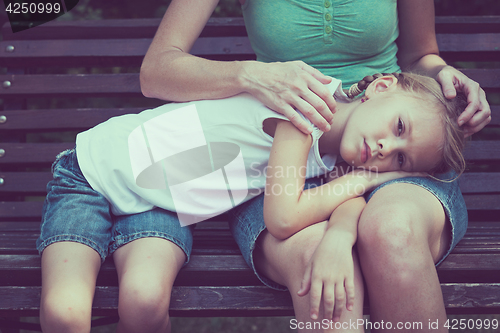 Image of Sad mother and daughter sitting on bench in the park