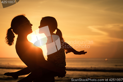 Image of Mother and daughter playing on the beach at the sunset time.