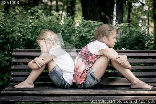 Image of two sad sister sitting on the bench in park