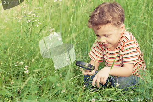 Image of Happy little boy exploring nature with magnifying glass