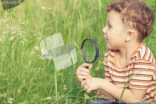 Image of Happy little boy exploring nature with magnifying glass