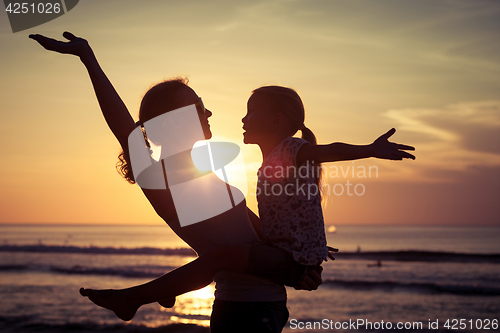 Image of Mother and daughter playing on the beach at the sunset time. 