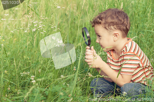 Image of Happy little boy exploring nature with magnifying glass