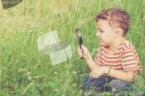 Image of Happy little boy exploring nature with magnifying glass