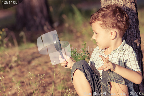 Image of Happy little boy exploring nature with magnifying glass