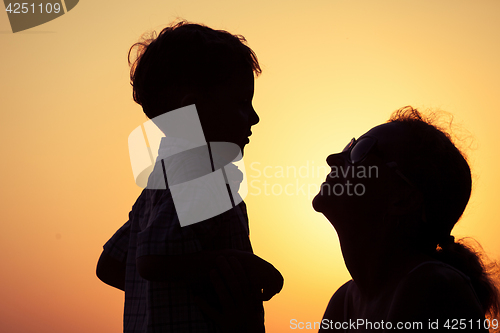 Image of Mother and son playing on the beach at the sunset time.