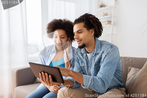 Image of happy couple with tablet pc and earphones at home