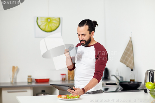 Image of man with tablet pc eating at home kitchen