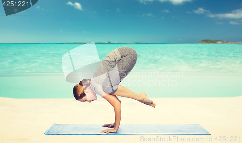 Image of woman making yoga in crane pose on mat over beach 