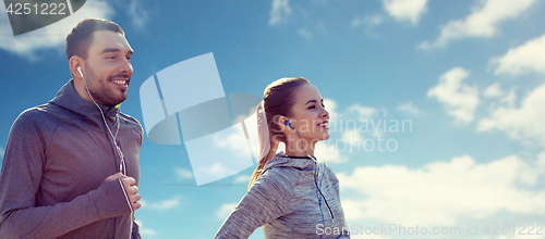 Image of happy couple with earphones running over blue sky