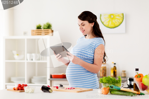 Image of pregnant woman with tablet pc cooking at home