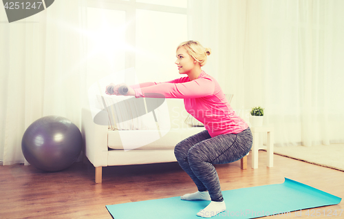 Image of smiling woman with dumbbells exercising at home