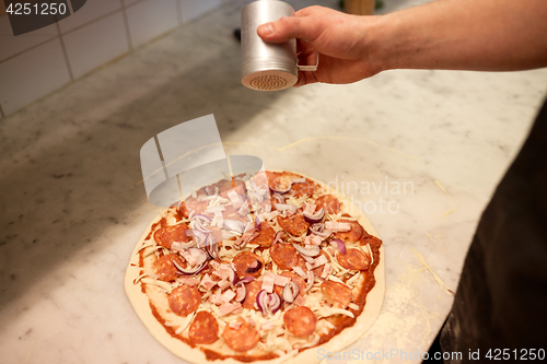 Image of cook adding pepper to salami pizza at pizzeria