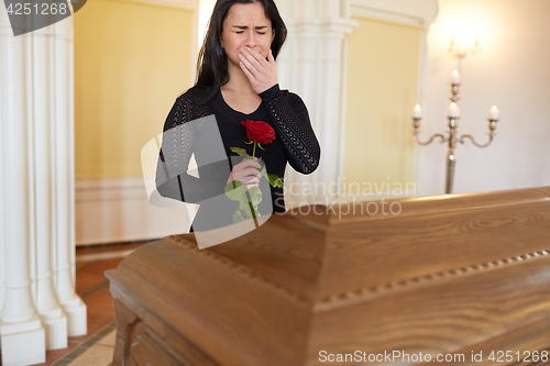 Image of crying woman with red rose and coffin at funeral