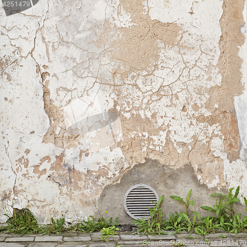 Image of abandoned cracked stucco wall with ventilation grille
