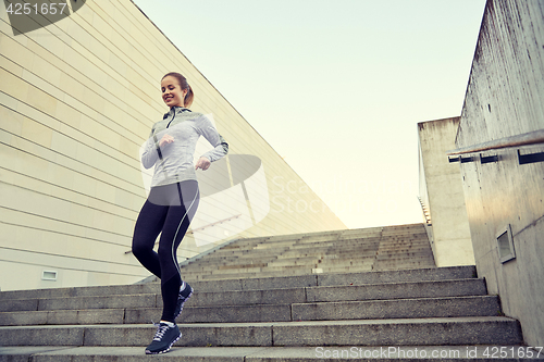 Image of happy sporty woman running downstairs in city