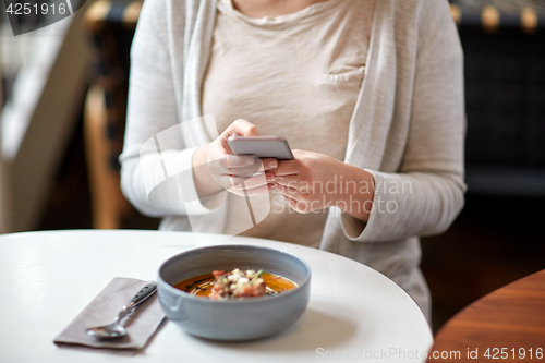 Image of woman with smartphone and pumpkin soup at cafe