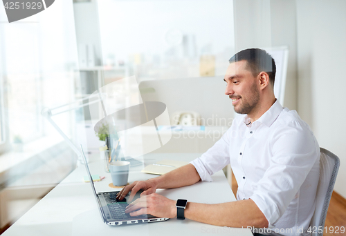 Image of happy businessman typing on laptop at office