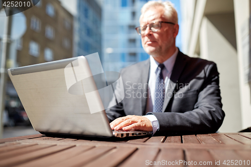 Image of senior businessman with laptop at outdoor cafe