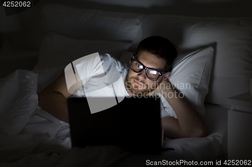 Image of young man with laptop in bed at home bedroom