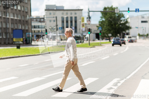 Image of senior man walking along city crosswalk