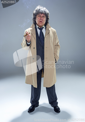 Image of The senior man with cigar as detective or boss of mafia on gray studio background