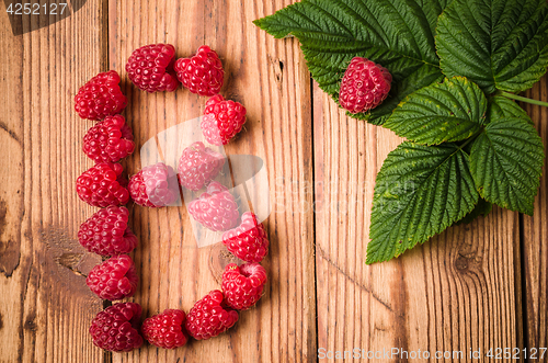 Image of Letter B of raspberries with leaves on a wooden surface, close-u