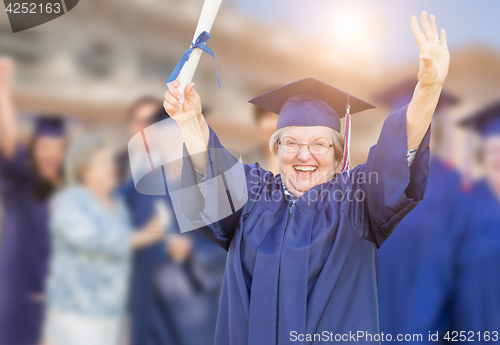 Image of Happy Senior Adult Woman In Cap and Gown At Outdoor Graduation C