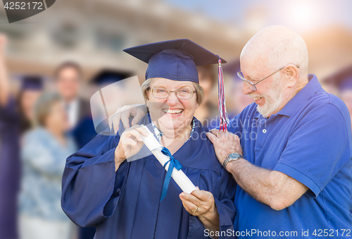 Image of Senior Adult Woman In Cap and Gown Being Congratulated By Husban