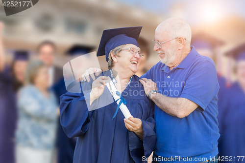 Image of Senior Adult Woman In Cap and Gown Being Congratulated By Husban