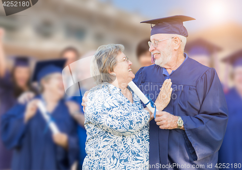 Image of Senior Adult Male In Cap and Gown Being Congratulated By Wife At