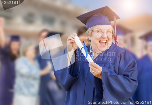 Image of Happy Senior Adult Woman In Cap and Gown At Outdoor Graduation C
