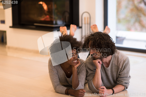 Image of multiethnic couple lying on the floor  in front of fireplace