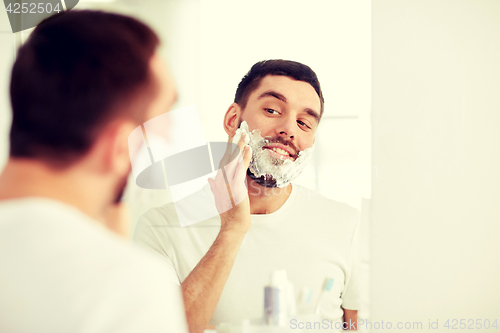 Image of happy man applying shaving foam at bathroom mirror