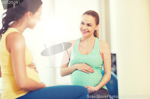 Image of two happy pregnant women sitting on balls in gym